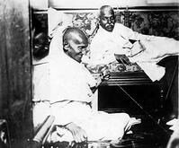 Mahatma Gandhi spinning in the cabin of Pundit Madan Mohan Malaviya (right) on board of S.S. Rajputana during his voyage to England, Bombay, August 1931. [AKG110392632]