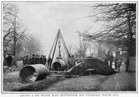 Photograph showing engineers and assistants lifting up heavy large circular piping with a crane ready to be put underground, in the streets of South London. [TPG110085089]