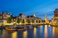 Boats moored along illuminated street on Amstel River and Munttoren tower at twilight, Amsterdam, Netherlands [AWL110002041]