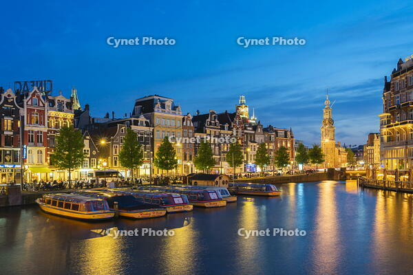 Boats moored along illuminated street on Amstel River and Munttoren tower at twilight, Amsterdam, Netherlands [AWL110002041]
