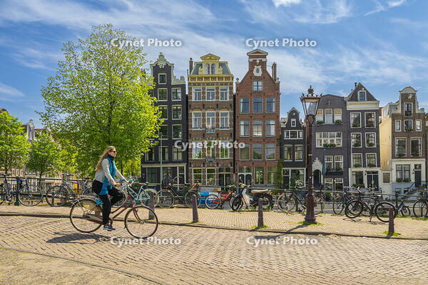 Woman riding bicycle on street with typical houses in background, Herengracht canal, Amsterdam, Netherlands [AWL110002044]