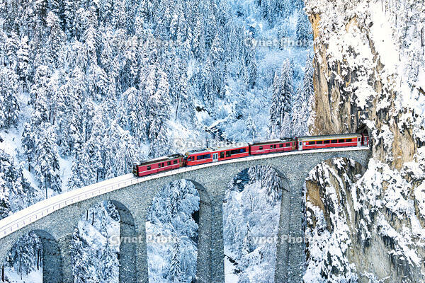Train on Landwasser viaduct entering in a tunnel carved into a mountain ridge in winter, Filisur, Graubunden canton, Switzerland [AWL110002252]