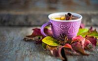 Autumnal concept with cup of tea with lemon, cinnamon stick and anise star on rustic wooden background full of bright yellow leaves [IBR123380126]