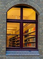 A view through the window of a library, shelves full of books illuminated by a warm, yellow light, Berlin, Germany [IBR112672613]