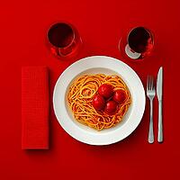 Pasta with tomatoes in a round plate on a red table, top view, AI generated [IBR123435199]