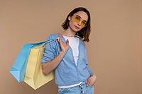 Confident fashion woman in casual clothing holding shopping bags spending time in mall isolated over beige background [IBR123569295]