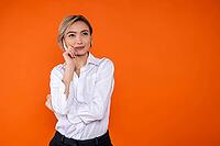 Pensive woman wearing white official style shirt thinking holding chin free space isolated over orange background [IBR123569296]