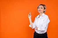 Confident happy woman wearing white official style shirt pointing at empty space isolated over orange background [IBR123569297]
