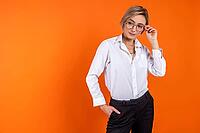 Serious woman wearing white official style shirt holding glasses looking away free space isolated over orange background [IBR123569304]