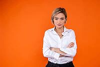 Serious confident woman wearing white official style shirt standing with arms folded isolated over orange background [IBR123569305]