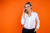 Smiling woman wearing white official style shirt talking on smartphone isolated over orange background [IBR123569306]