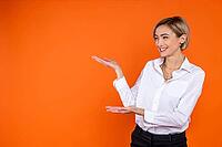 Satisfied woman wearing white official style shirt showing empty space on palm isolated over orange background [IBR123569308]