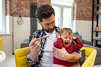 Little child care. Father feeding crying capricious infant daughter sitting at home in modern interior [IBR123569316]