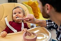 Little baby eating her dinner with dad, unrecognizable father feeding toddler kid, first lure [IBR123569318]