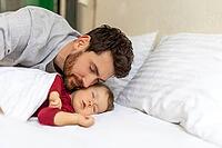 Handsome brunette father kissing sleeping infant baby tenderly home interior [IBR123569321]