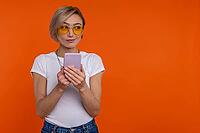 Cunning sly woman wearing white T-shirt using mobile phone checking social networks isolated over orange background [IBR123569325]