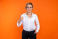 Attractive confident woman wearing white official style shirt showing thumb up isolated over orange background [IBR123569326]