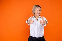 Positive woman wearing white official style shirt showing like gesture and winking to camera isolated over orange background [IBR123569328]