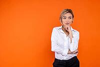 Pensive thoughtful woman wearing white official style shirt thinking holding chin isolated over orange background [IBR123569336]