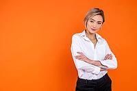 Confident woman wearing white official style shirt standing with crossed arms looking at camera isolated over orange background [IBR123569339]