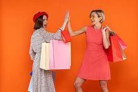 Happy women friends with shopping bags giving high five isolated over orange background [IBR123569340]