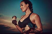 Young sports woman training with dumbbells on twilight sky background, tattoo on hand [IBR123569355]