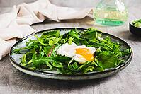 Poached egg in arugula and chard leaves on a plate on a table [IBR123629690]