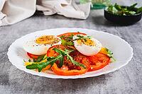 Light appetizer of tomatoes, boiled egg, cheese and arugula on a plate on the table [IBR123629699]
