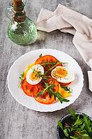 Tomato slices, egg, cheese and herbs on a plate on the table vertical view [IBR123629702]