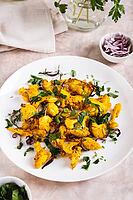 Baked spicy cauliflower with onions and parsley on a plate on the table vertical view [IBR123629703]