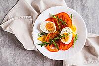 Close up of light appetizer of tomatoes, boiled egg, cheese and arugula on a plate top view [IBR123629725]