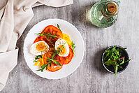 Light appetizer of tomatoes, boiled egg, cheese and arugula on a plate top view [IBR123629726]
