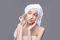 Young asian female applying under eye patches for skincare routine with towel wrapped around head [IBR123629735]