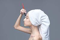 Young caucasian female applying makeup with brush and towel wrapped on her head [IBR123629741]