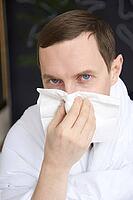 Caucasian adult male with cold symptoms using tissue for sneezing relief indoors [IBR123629742]
