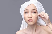 Young caucasian female applying eye patch with towel wrapped hair in skincare routine [IBR123629743]