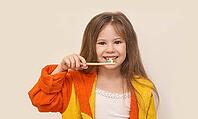 Caucasian young girl brushing teeth with colorful toothbrush in yellow orange bathrobe smiling healthy hygiene [IBR123629752]