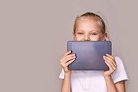 Smiling caucasian young female child holding tablet against beige background [IBR123629755]