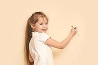 Caucasian female child painting wall with brush smiling long hair creative activity [IBR123629756]