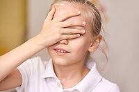 Young caucasian girl covering eyes with hand wearing white polo shirt indoors [IBR123629757]