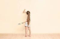 Young caucasian girl painting wall with brush in minimalistic room interior [IBR123629764]