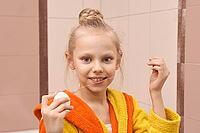 Caucasian female child flossing teeth in bathroom wearing yellow and orange bathrobe [IBR123629765]