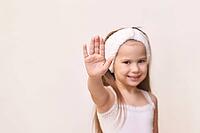Young caucasian female child with headband making hand gesture against neutral background [IBR123629766]