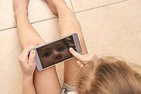 Young caucasian child engaged with smartphone technology reflection on screen [IBR123629769]