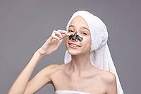 Young caucasian female applying blackhead mask with towel on head smiling skincare routine [IBR123629772]