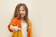 Caucasian young girl in orange bathrobe holding toothbrush with multicolored toothpaste [IBR123629774]