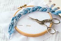 Embroidery tools and materials, wooden hoop, blue embroidery floss, metal scissors, and needles on white fabric, arranged for needlework and crafting, cross stitch concept [IBR123638364]