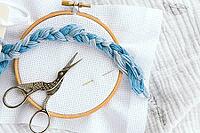 Embroidery hoop with white canvas, braid of blue thread, stork-shaped scissors and needles on soft textile background, representing craftsmanship, patience and creativity, cross stitch concept [IBR123638372]
