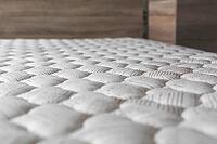 Close-up of white textured mattress surface with soft quilted pattern, in cozy bedroom interior with wooden furniture, concept of comfort, sleep and relaxation [IBR123638374]