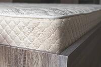 Comfortable orthopedic mattress with a quilted surface on a wooden bed frame, showcasing high-quality fabric texture and ergonomic design for restful sleep [IBR123638380]